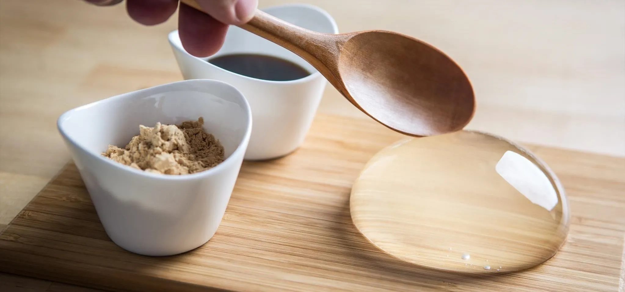 Bowl of brown sugar and soy sauce with a wooden spoon on a wooden surface.