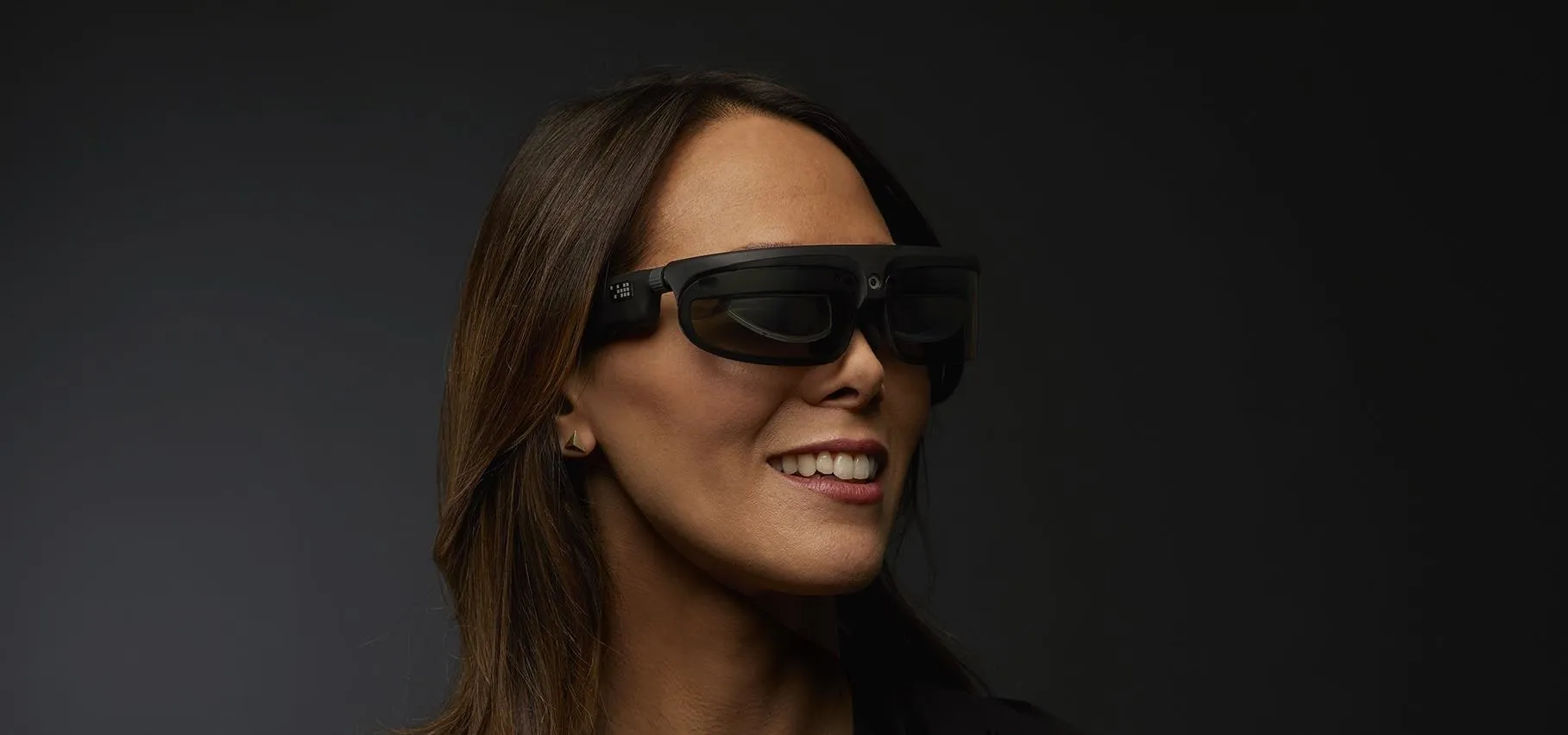 Woman wearing modern smart glasses against a dark background.