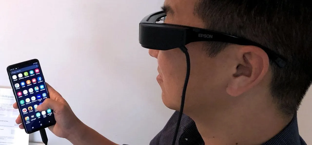 A person using smart glasses while holding a smartphone.