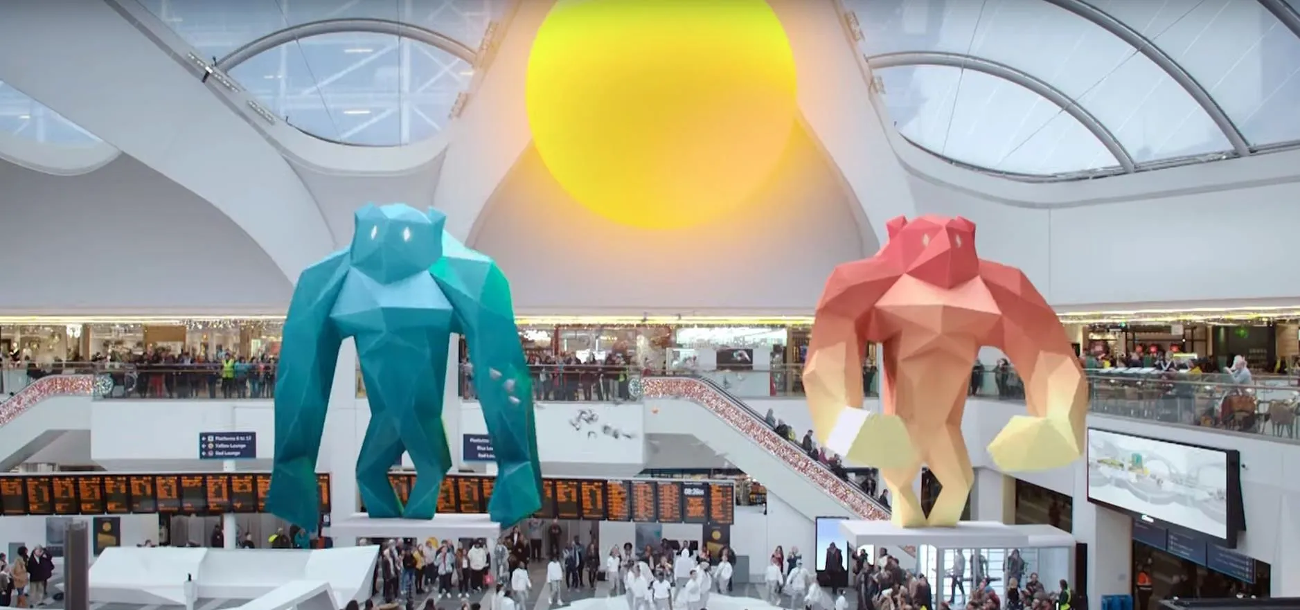 Art installations of large colorful figures in a bright, modern indoor space with a crowd.