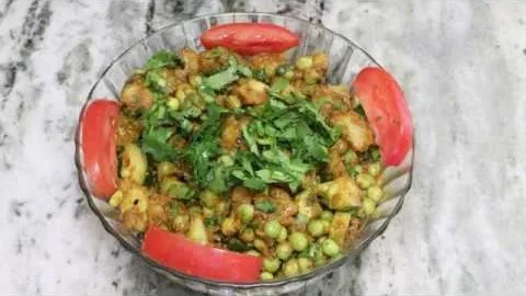 Bowl of mixed vegetables with peas, garnished with tomato slices and fresh cilantro.